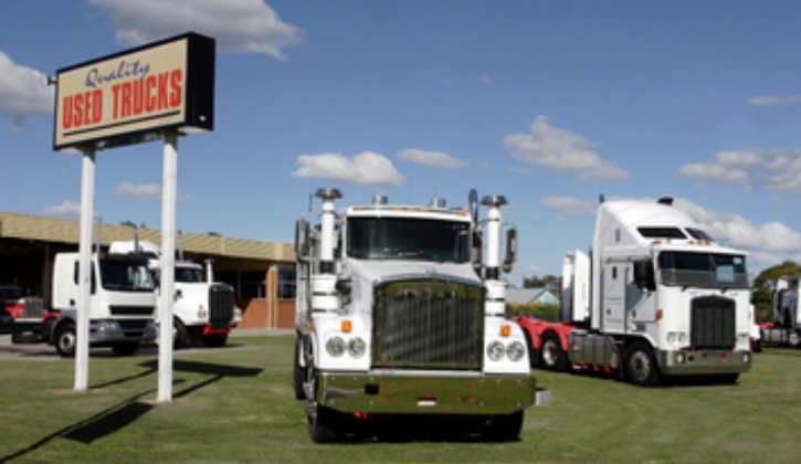 Used truck dealership. Several trucks parked in the grass next to a Quality Used Trucks sign.