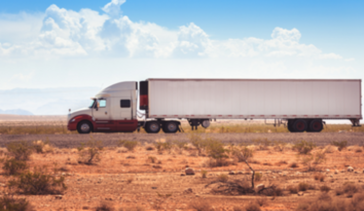 White semi truck with a red stripe pulling a trailer through the desert