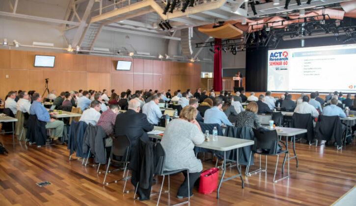 View of seminar from the back, showing rows of people at tables watching the stage